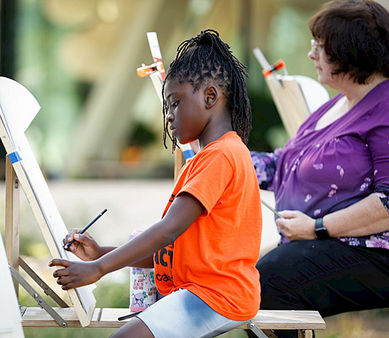 Photo of a young girl and older woman drawing at art easels.