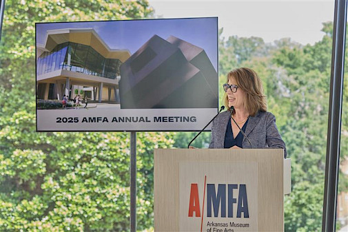 Photo of Dr. Victoria Ramirez speaking at a podium with a screen behind her displaying a photo of the Arkansas Museum of Fine Arts with the words 2025 AMFA Annual Meeting.