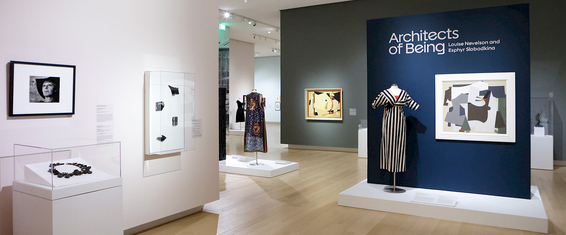 Photo of an art gallery displaying abstract paintings, dresses, jewelry, and photographs.