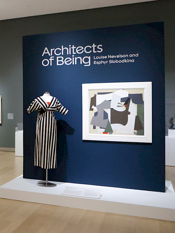 Photo of an art gallery displaying abstract paintings, dresses, jewelry, and photographs.