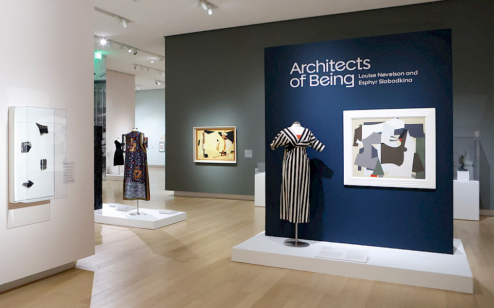 Photo of an art gallery displaying abstract paintings, dresses, jewelry, and photographs.