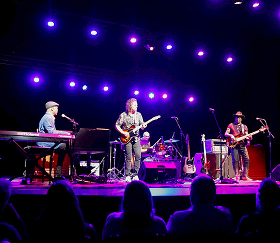 Photo of a band playing on a stage lit with purple lights.